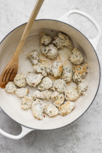 Chicken pieces being cooked in a white pot with a wooden spoon.