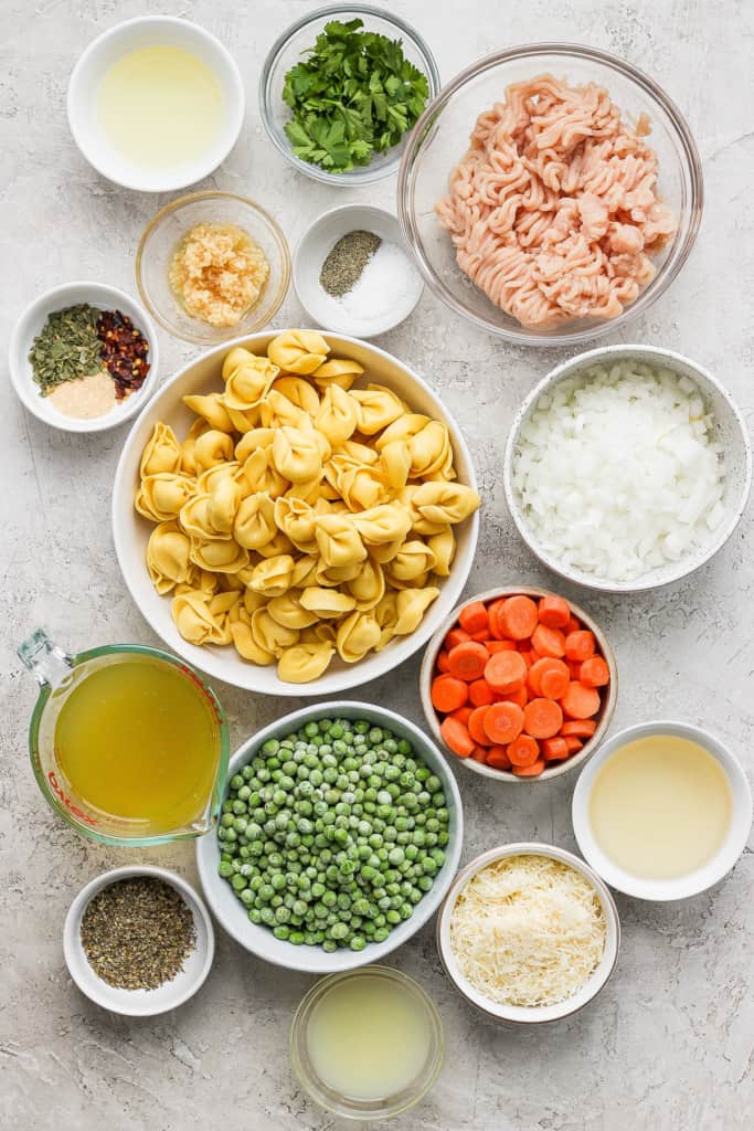 Assorted ingredients for cooking laid out on a surface, including pasta, vegetables, ground meat, spices, and broth.