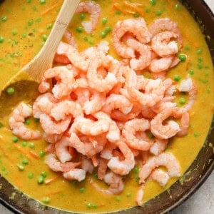 A skillet filled with a creamy pea soup topped with a mound of cooked shrimp, with a wooden spoon resting inside the pan.