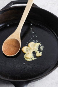 A wooden cooking spoon rests on a black cast iron skillet with remnants of cooked food.