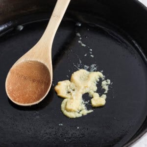 A wooden cooking spoon rests on a black cast iron skillet with remnants of cooked food.