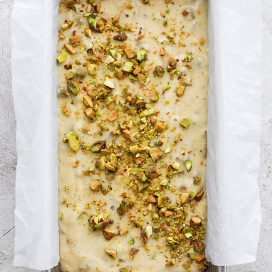 Unbaked dough in a metal tray topped with chopped nuts, prepared for baking and lined with parchment paper.
