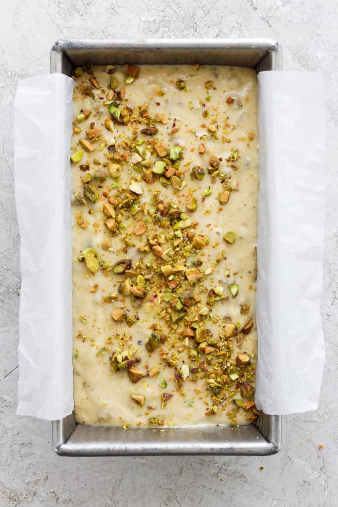 Unbaked dough in a metal tray topped with chopped nuts, prepared for baking and lined with parchment paper.
