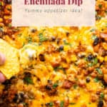 Close-up of baked enchilada dip with a chip scooping a serving, with text overlay stating "baked enchilada dip - yummy appetizer idea!.