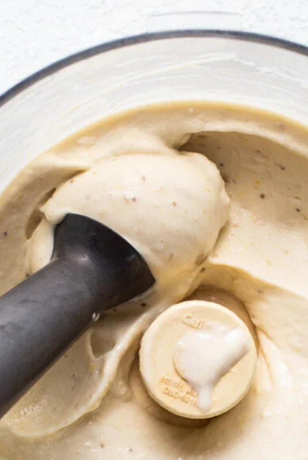 A blender filled with creamy banana nice cream, with a black tamper blending the mixture.