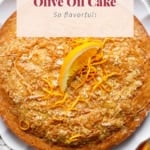 A freshly baked orange olive oil cake garnished with orange zest on a white plate.