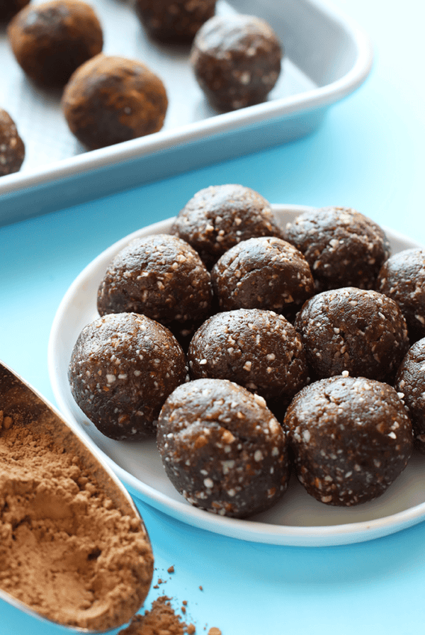 A plate of peanut butter brownie energy balls with a scoop of cocoa powder on the side.