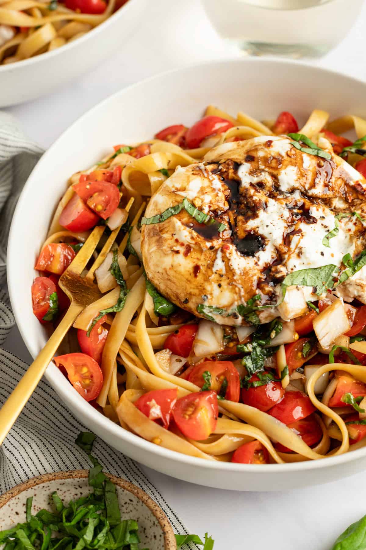 A bowl of fettuccine pasta topped with a grilled chicken breast, cherry tomatoes, and basil, drizzled with a creamy sauce.