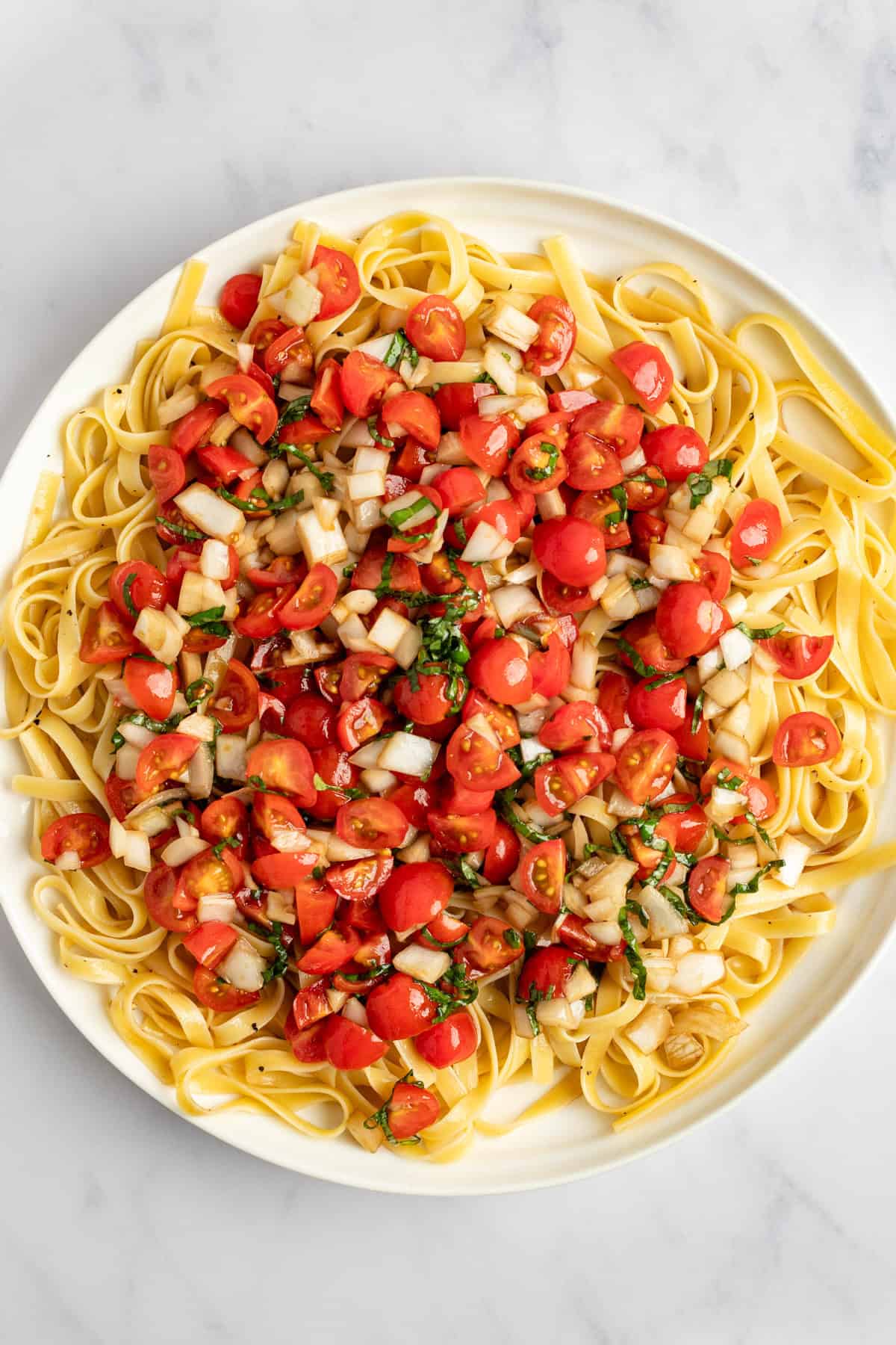 A plate of fettuccine pasta topped with chopped tomatoes, onions, and herbs.