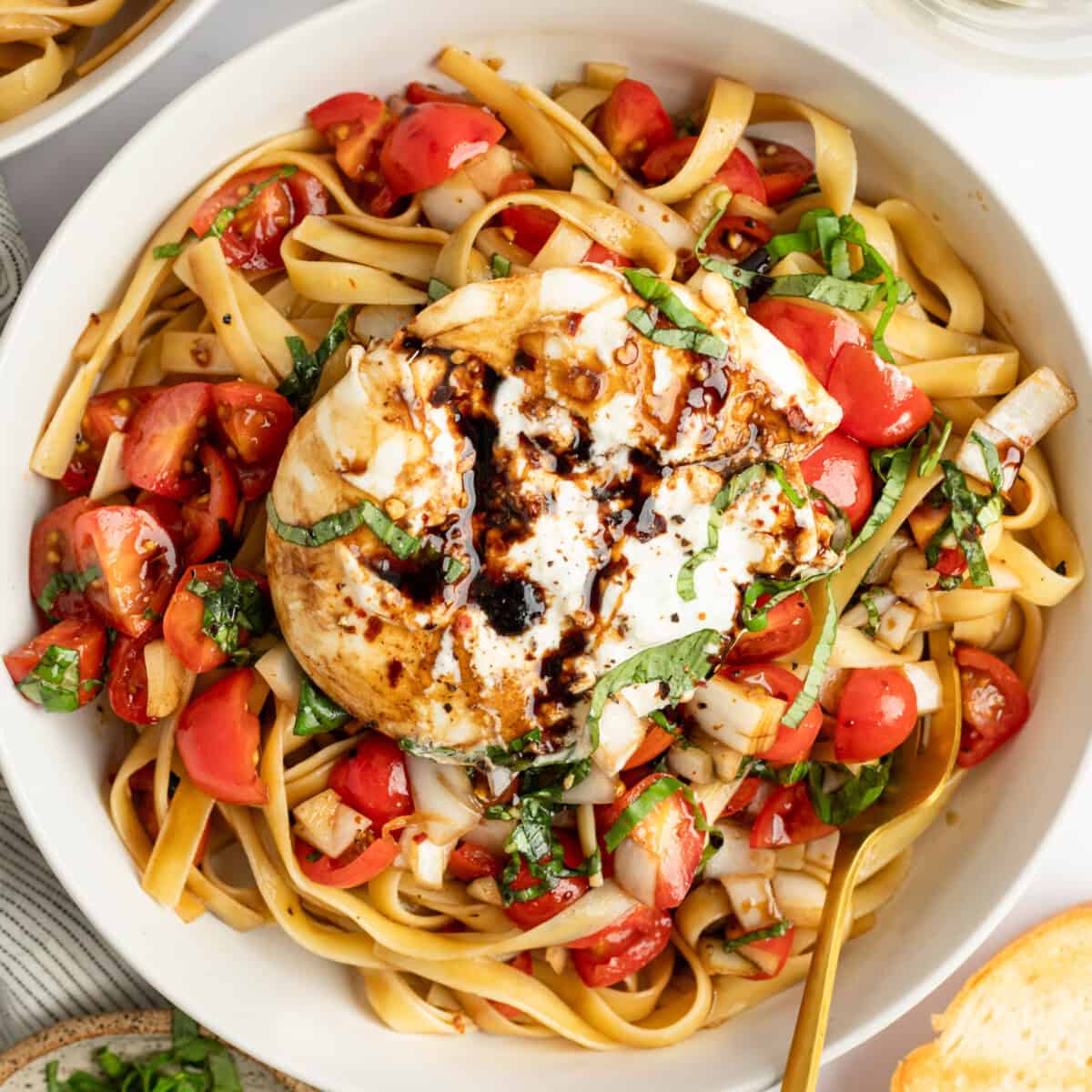 A vessel  of pasta with tomatoes, caller  basil, and a ample  mozzarella shot  drizzled with balsamic glaze.