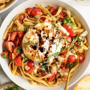 A bowl of pasta with tomatoes, fresh basil, and a large mozzarella ball drizzled with balsamic glaze.