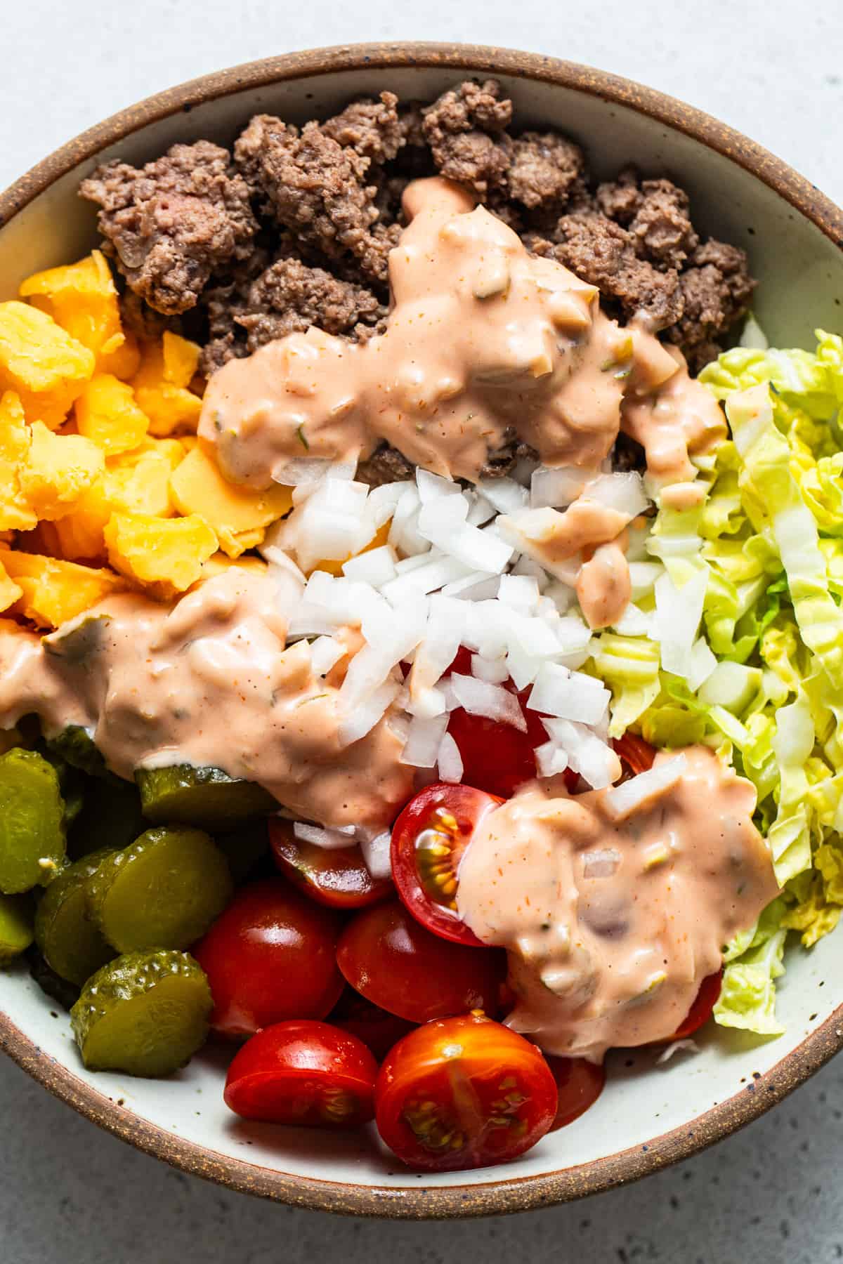 A bowl of salad with diced tomatoes, chopped lettuce, onions, pickles, ground meat, and drizzled with creamy dressing.