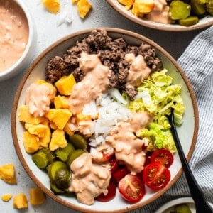 A bowl of salad with ground beef, rice, lettuce, tomatoes, pickles, olives, and diced mango, topped with a creamy dressing.