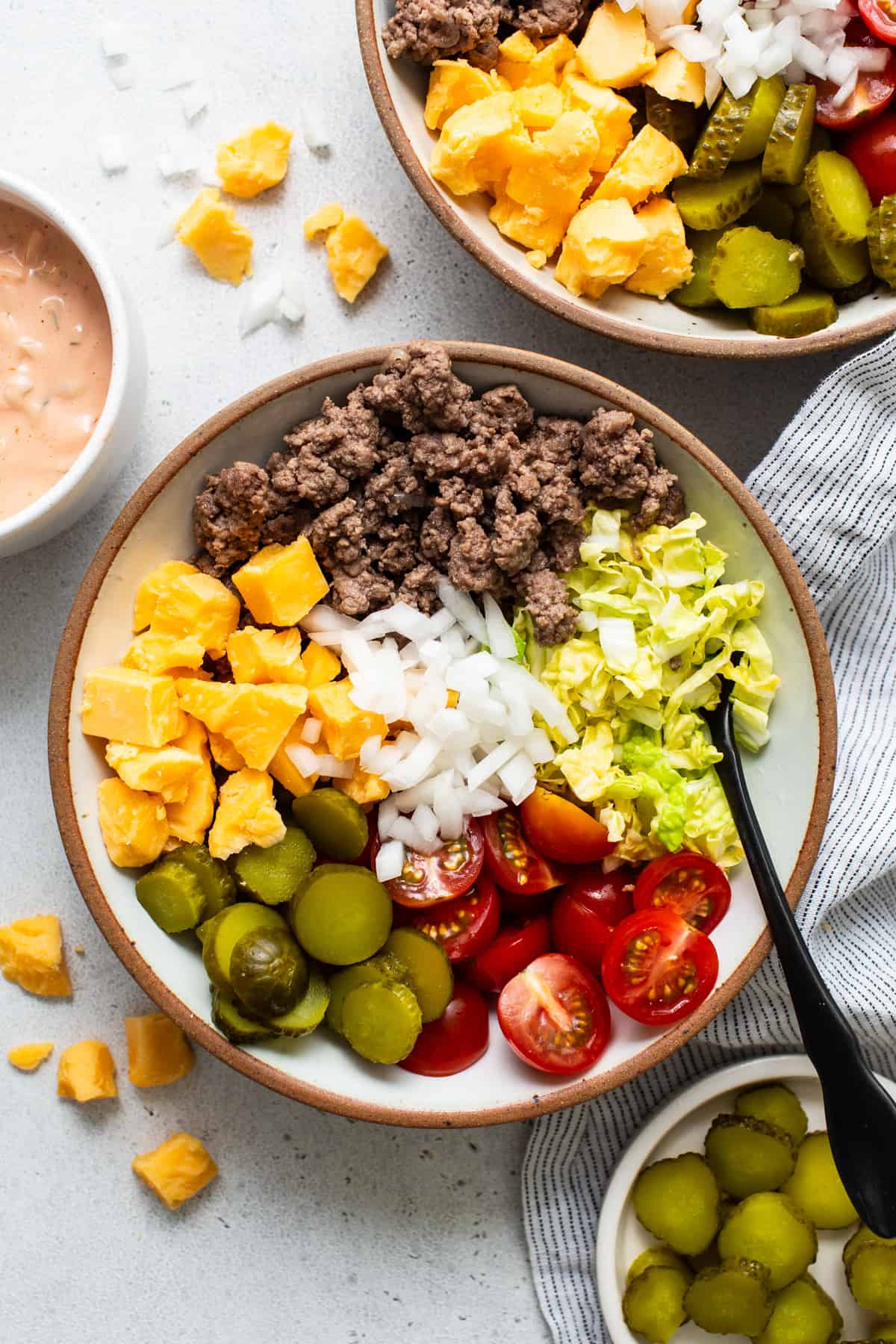 A salad bowl featuring sections of ground beef, chopped tomatoes, onions, cheese, lettuce, and olives, with a side of dressing.