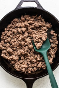 Cooked ground beef in a black cast iron skillet with a green spatula.
