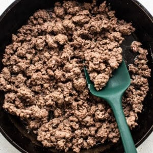 Cooked ground beef in a black cast iron skillet with a green spatula.