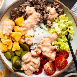 A bowl of salad with ground beef, diced mango, onions, lettuce, cherry tomatoes, jalapeños, and a drizzle of creamy dressing.