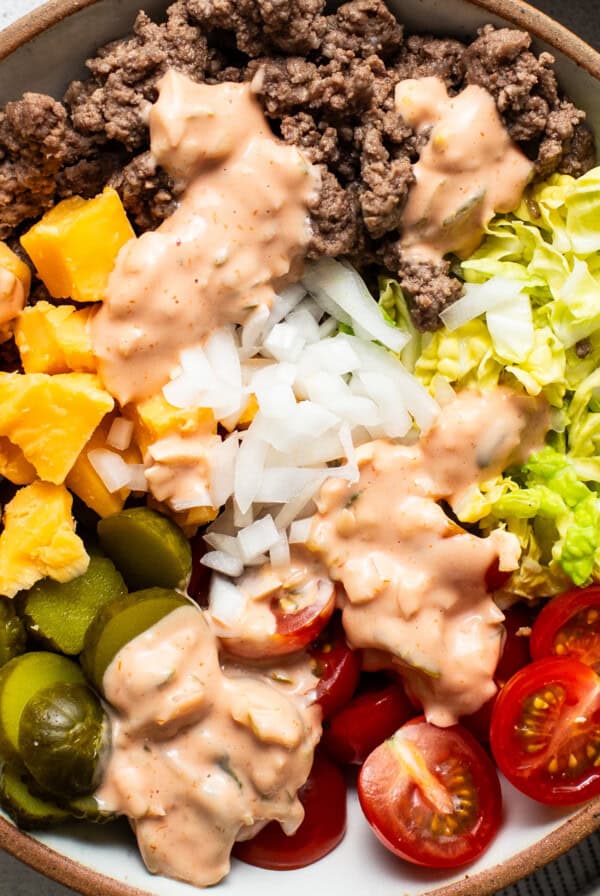 A bowl of salad with ground beef, diced mango, onions, lettuce, cherry tomatoes, jalapeños, and a drizzle of creamy dressing.