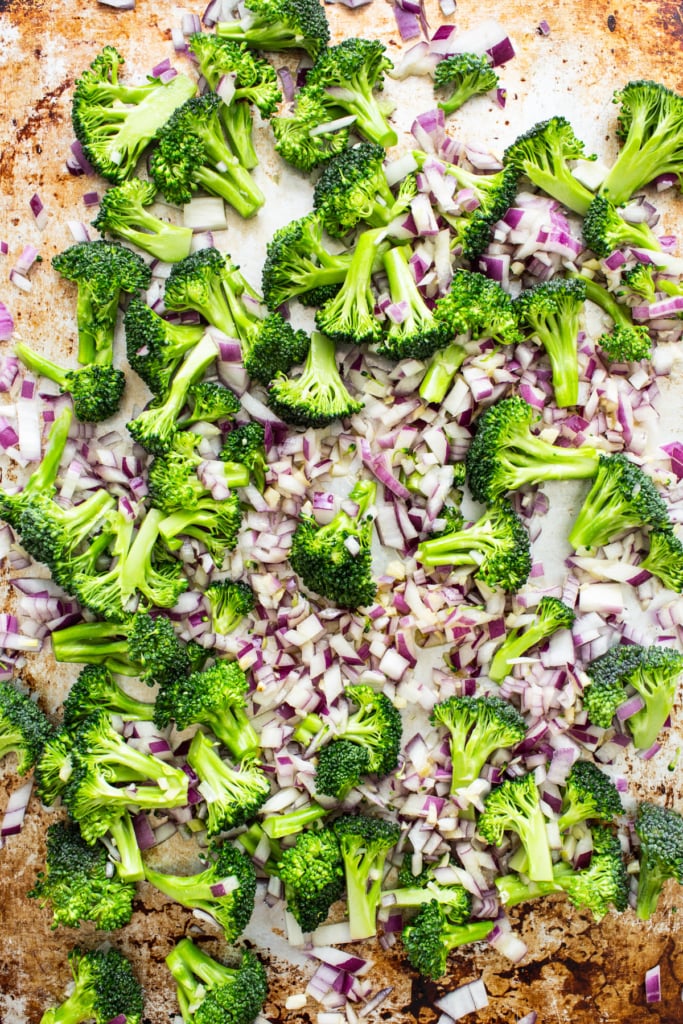 Chopped broccoli and red onions spread on a baking sheet, ready for roasting.