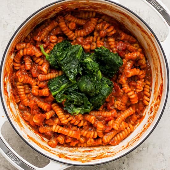 Pasta with tomato sauce and spinach in a white pot.