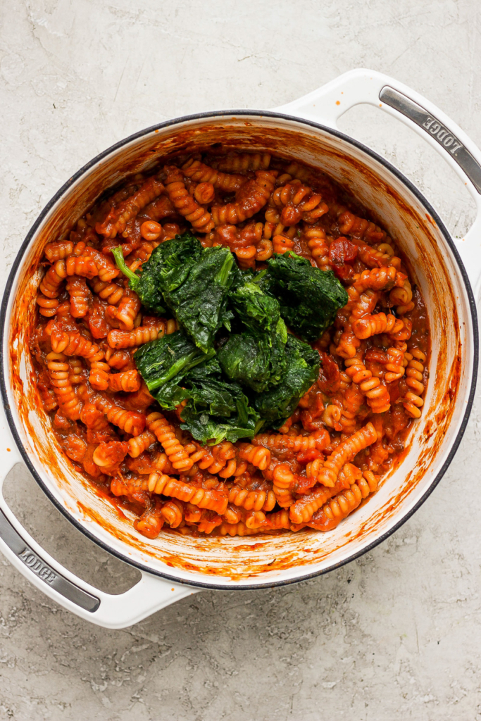 Pasta with tomato sauce and spinach in a white pot.