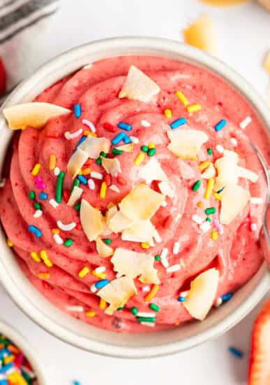 A vibrant pink smoothie bowl topped with coconut flakes and colorful sprinkles, viewed from above.