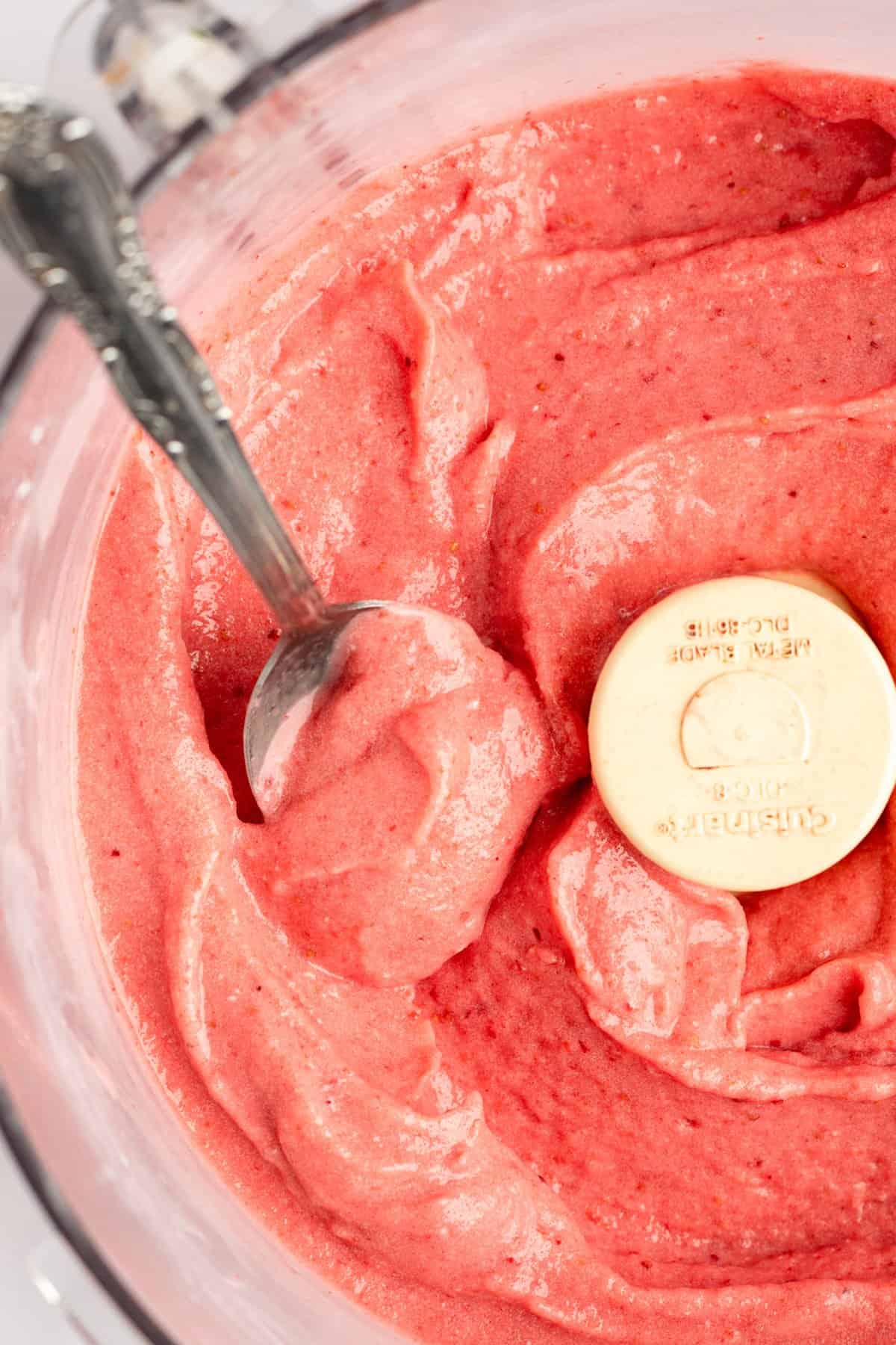 Top-down view of a bowl of fresh strawberry puree with a measuring spoon dipped inside.