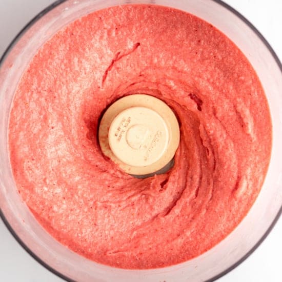 Top view of a food processor containing freshly blended strawberry puree.