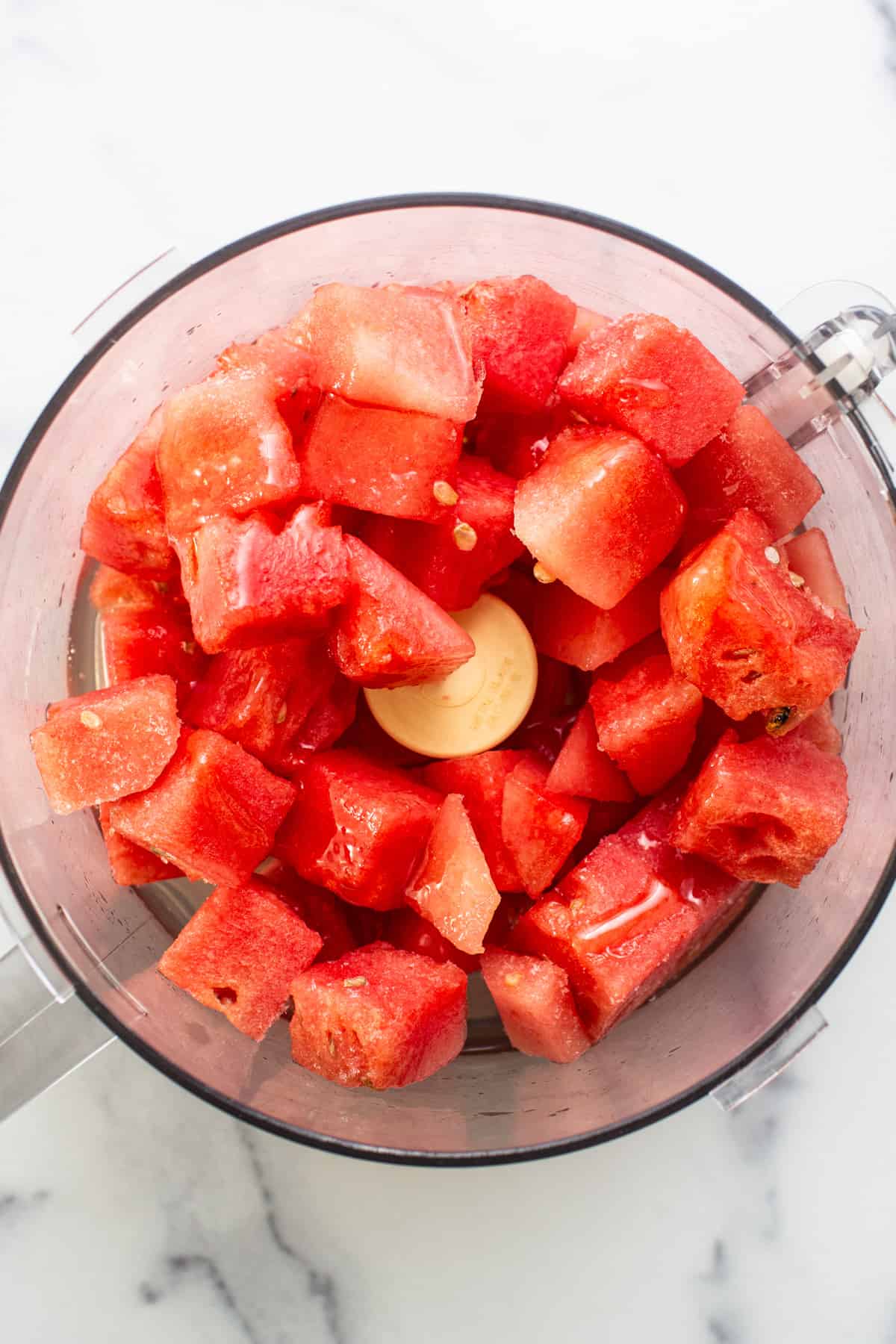 Chunks of fresh red watermelon in a food processor, ready for blending.