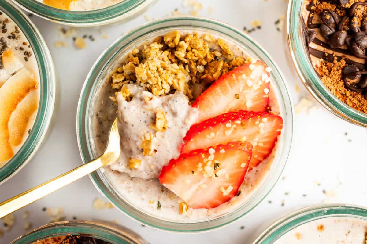 A bowl of oatmeal topped with sliced strawberries, granola, and a gold spoon placed in it.