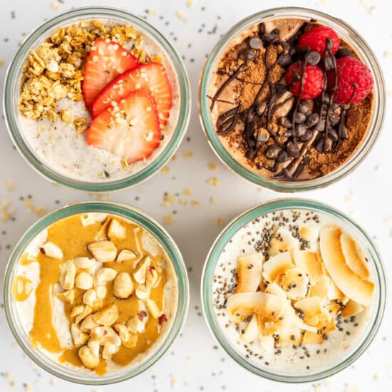Top-down view of four jars filled with different flavors of overnight oats, garnished with toppings like strawberries, chocolate, raspberries, nuts, and coconut flakes, arranged in a 2x2 grid.