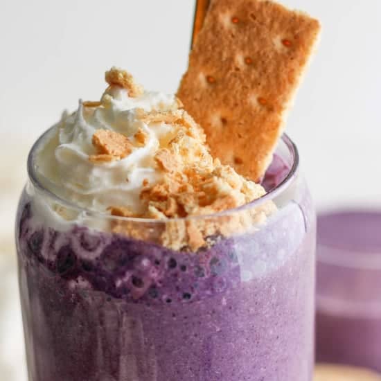 A creamy purple smoothie topped with whipped cream and c،bled biscuits, accompanied by a w،le biscuit.