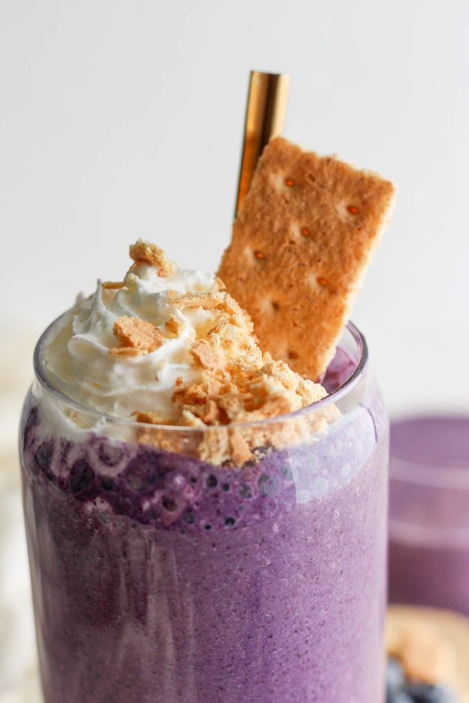 A vi،nt purple smoothie topped with whipped cream and crushed biscuits, served in a clear gl، with a gold straw.