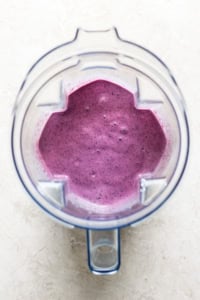 Top view of a blender jug filled with freshly blended purple smoothie, situated on a light-colored background.