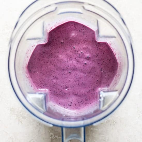 Top view of a blender jug filled with freshly blended purple smoothie, situated on a light-colored background.
