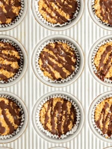 A baking sheet with nine muffin tin liners filled with a mixture topped with drizzled chocolate.