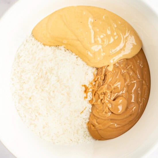 A bowl containing shredded coconut, smooth peanut butter, and crunchy peanut butter.