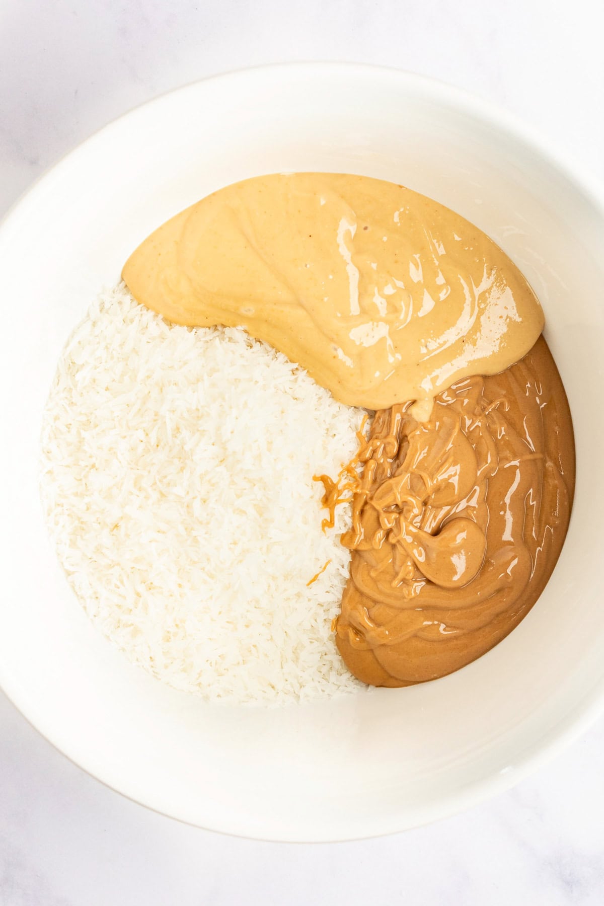 A bowl containing shredded coconut, smooth peanut butter, and crunchy peanut butter.