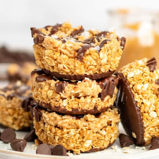 A stack of three granola clusters coated with chocolate. They are topped with flakes of salt and surrounded by chocolate chips.
