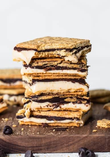 A stack of s'mores with melted chocolate and marshmallows, surrounded by cookie crumbs and chocolate chips.