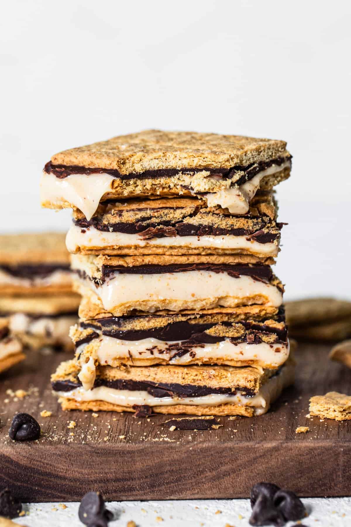 A stack of s'mores with melted chocolate and marshmallows, surrounded by cookie crumbs and chocolate chips.