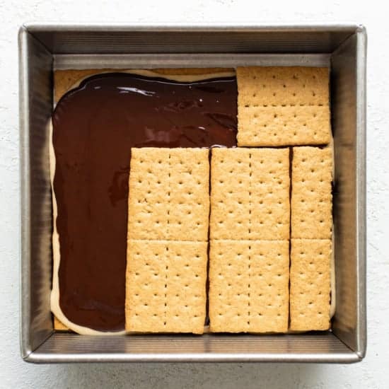 A baking dish with a layer of chocolate topped by aligned graham crackers, preparing for a s'mores dessert.