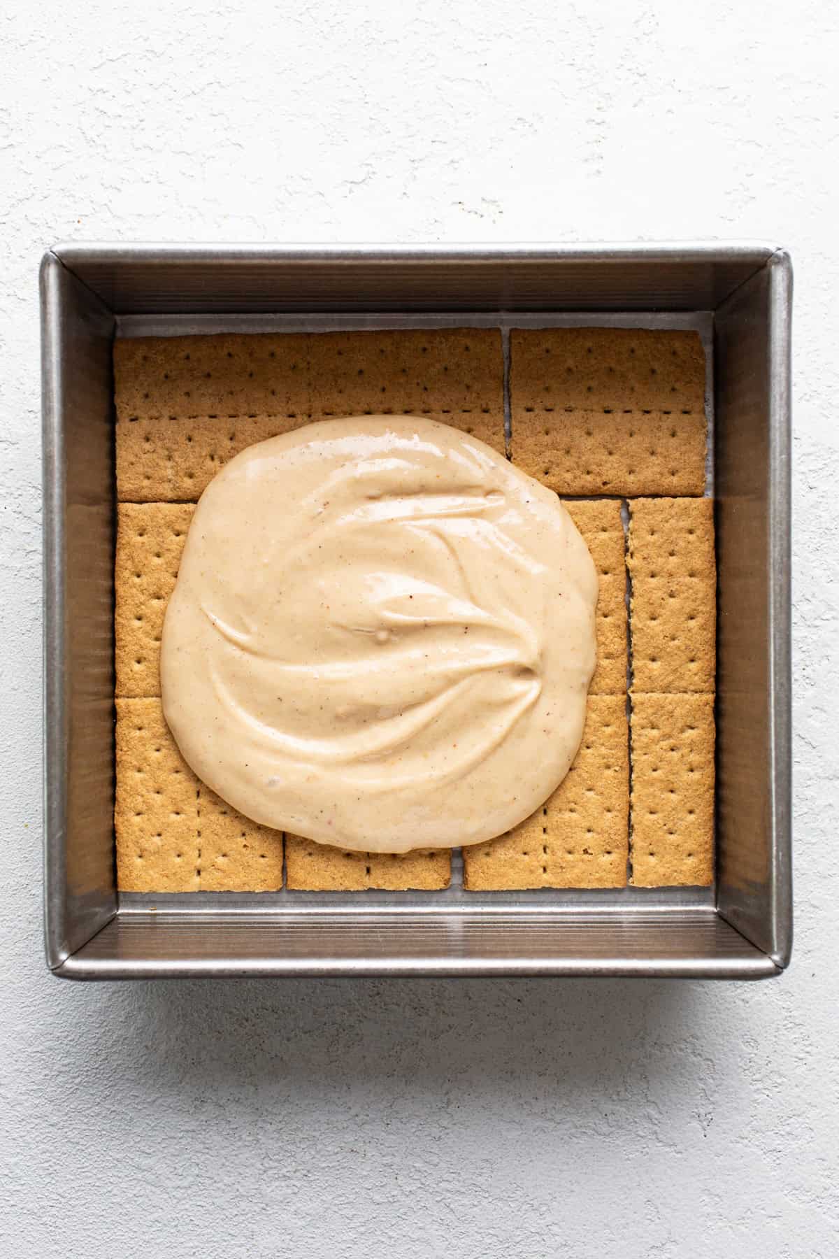 A square baking dish filled with graham crackers topped with a layer of smooth, creamy filling.