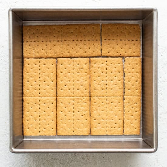 Rectangular graham crackers neatly arranged in a metal baking tray on a white textured background.
