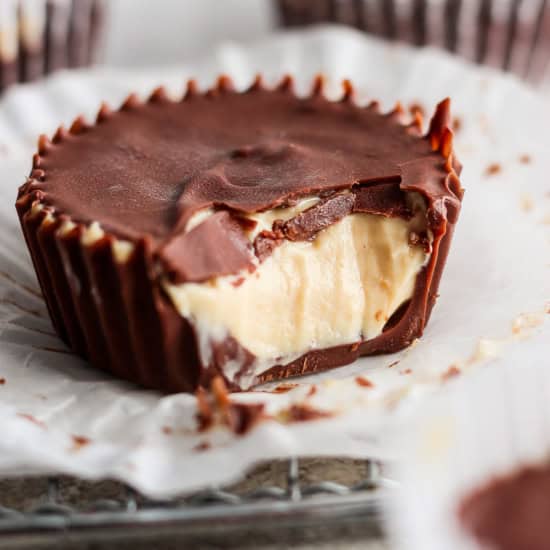 A close-up image of a chocolate peanut butter cup with a bite taken out, revealing creamy peanut butter filling. other cups in the background.