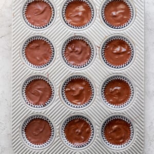 A tray of freshly baked chocolate muffins in paper liners, organized in a 4x3 grid, on a white textured surface.