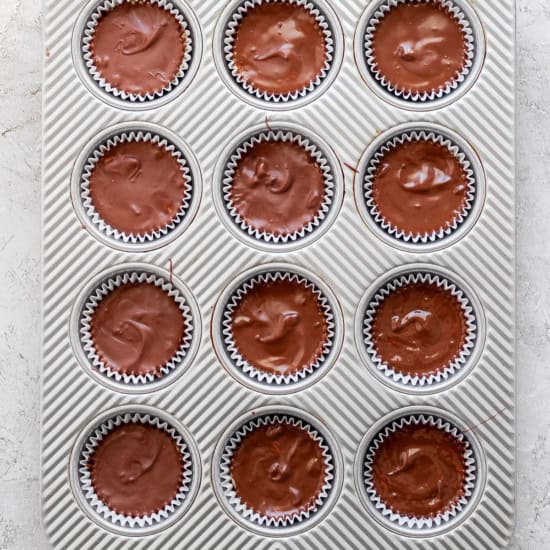 A tray of freshly baked chocolate muffins in paper liners, organized in a 4x3 grid, on a white textured surface.