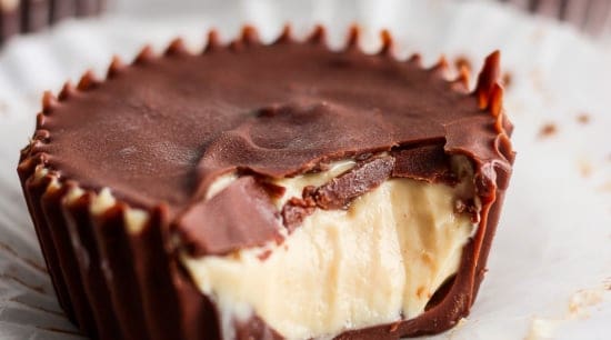 A close-up of a peanut butter cup with a bite taken out, revealing creamy peanut butter filling and a thick chocolate shell.