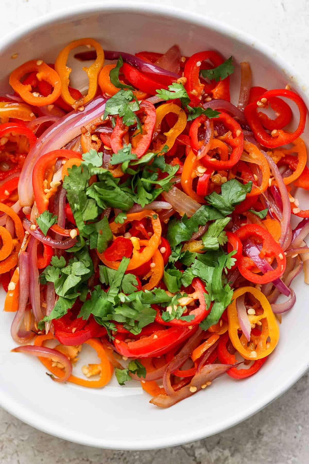 A bowl of sliced red onions, red and orange bell peppers, garnished with fresh cilantro.