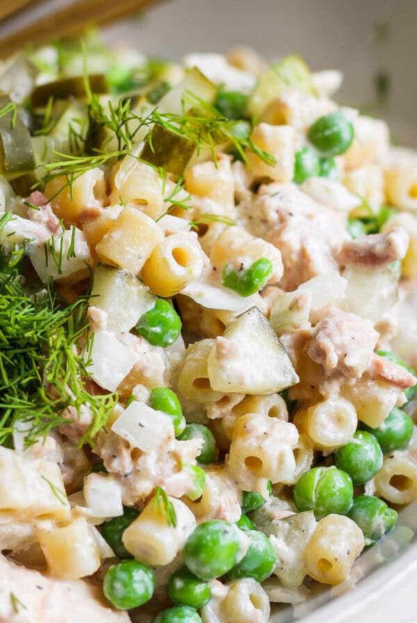 A close-up image of a creamy pasta salad with peas, chopped pickles, and fresh dill garnish in a bowl.
